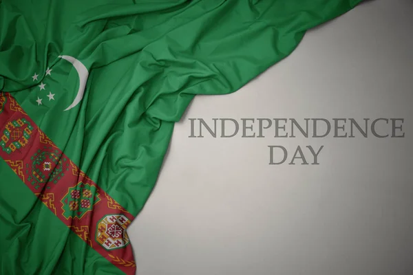 Machając kolorowe flagi narodowej Turkmenistanu na szarym tle z dniem niepodległości tekstu. — Zdjęcie stockowe