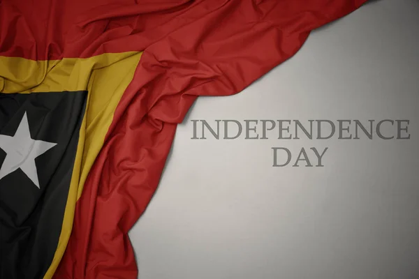 Acenando bandeira nacional colorida de timor leste em um fundo cinza com dia de independência de texto . — Fotografia de Stock