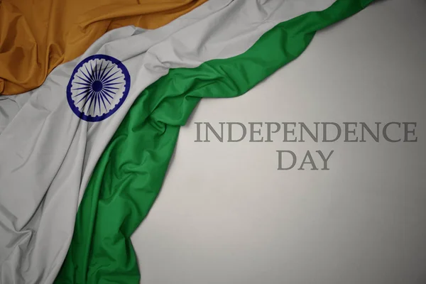 Zwaaiende kleurrijke nationale vlag van India op een grijze achtergrond met tekst Independence Day. — Stockfoto