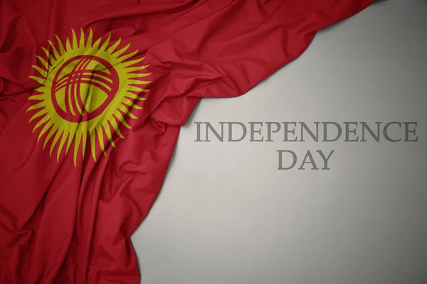 Machając kolorowe flagi narodowej Kirgistanu na szarym tle Dzień Niepodległości tekstu. — Zdjęcie stockowe
