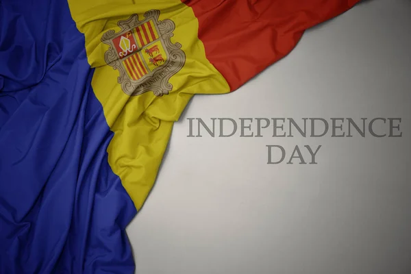 Zwaaiende kleurrijke nationale vlag van Andorra op een grijze achtergrond met tekst Independence Day. — Stockfoto