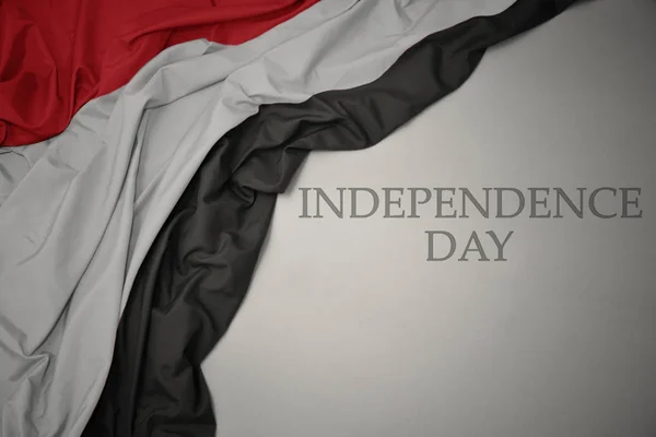 Zwaaiende kleurrijke nationale vlag van Jemen op een grijze achtergrond met tekst Independence Day. — Stockfoto