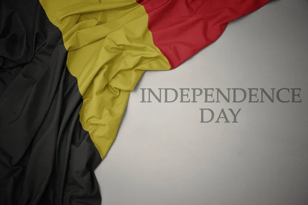 waving colorful national flag of belgium on a gray background with text independence day.