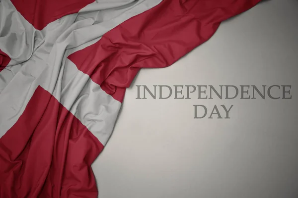 Hullámzó színes nemzeti zászló Dánia, a szürke háttér szöveg függetlenség napja. — Stock Fotó