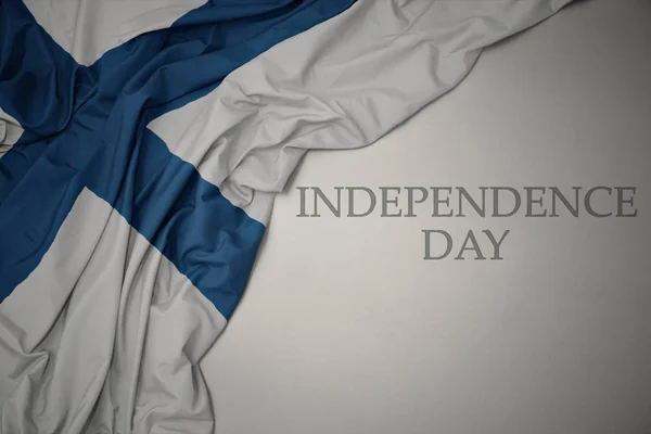 Machając kolorowe flagi narodowej Finlandii na szarym tle z dniem niepodległości tekstu. — Zdjęcie stockowe