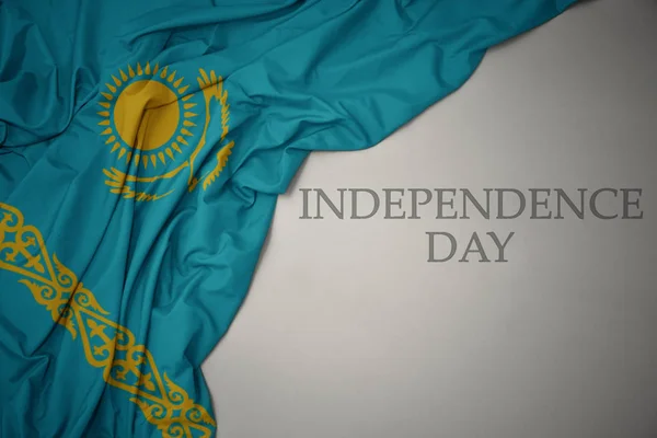 Hullámzó színes nemzeti zászló Kazahsztán egy szürke háttér szöveges függetlenség napja. — Stock Fotó