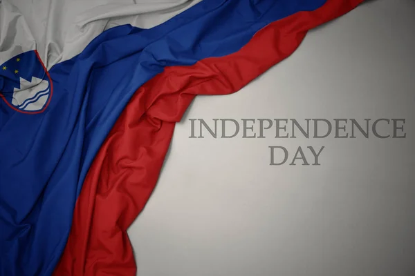 Machając kolorowe flagi narodowej Słowenii na szarym tle z dniem niepodległości tekstu. — Zdjęcie stockowe