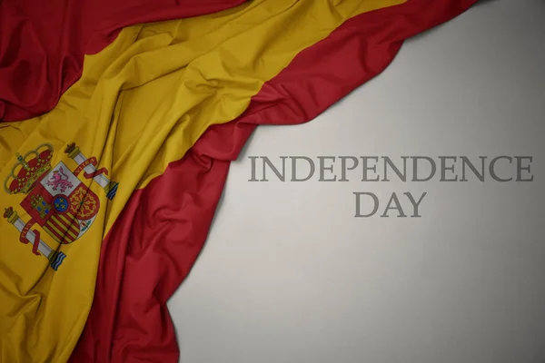 Zwaaiende kleurrijke nationale vlag van Spanje op een grijze achtergrond met tekst Independence Day. — Stockfoto