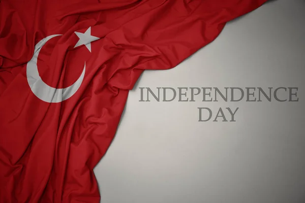 Machając kolorowe flagi narodowej Turcji na szarym tle z dniem niepodległości tekstu. — Zdjęcie stockowe
