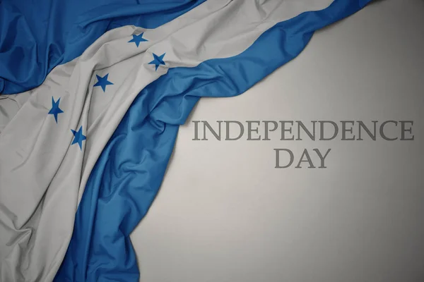 Sventolando bandiera nazionale colorata di honduras su uno sfondo grigio con il giorno dell'indipendenza del testo . — Foto Stock