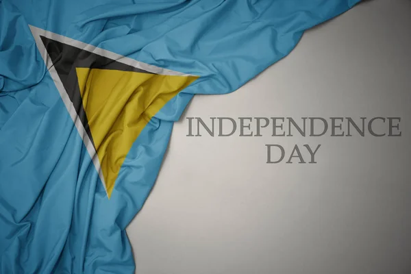 Hullámzó színes nemzeti zászló Szent Lucia a szürke háttér szöveges függetlenség napja. — Stock Fotó