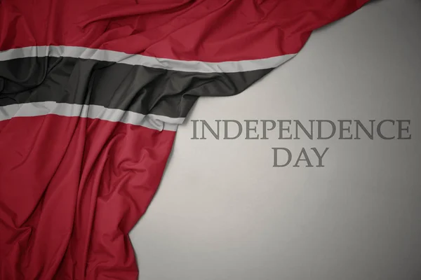 Színes hullámzó nemzeti zászló Trinidad és Tobago egy szürke háttér szöveg függetlenség napja. — Stock Fotó