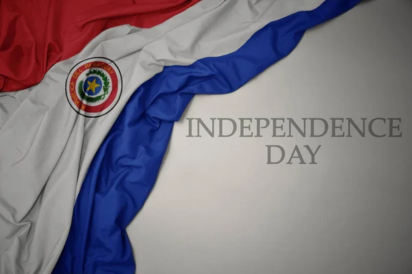 Κουνώντας τη πολύχρωμη εθνική σημαία της Παραγουάη σε γκρίζο φόντο με την ημέρα ανεξαρτησίας του κειμένου. — Φωτογραφία Αρχείου