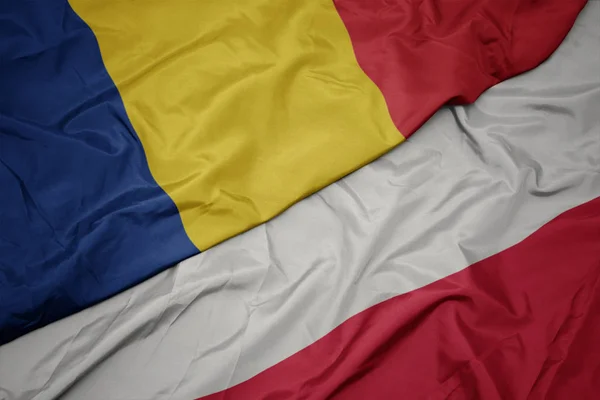 Zwaaiende kleurrijke vlag van Polen en de nationale vlag van Roemenië. — Stockfoto
