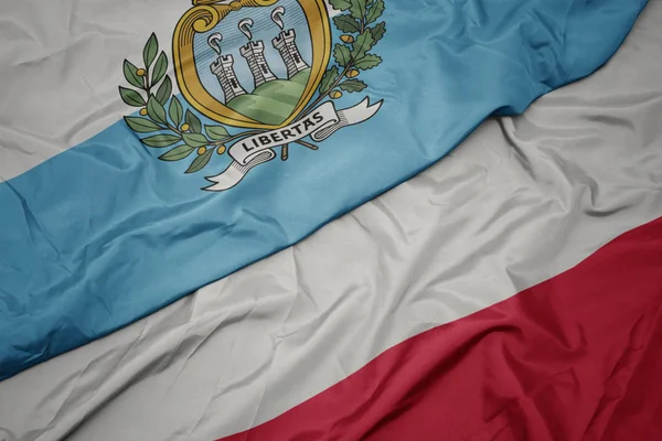 Zwaaiende kleurrijke vlag van Polen en de nationale vlag van San Marino. — Stockfoto