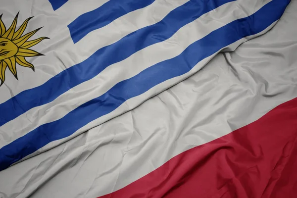 Ondeando colorida bandera de Polonia y bandera nacional de uruguay . —  Fotos de Stock