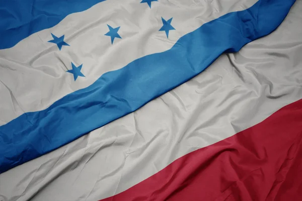 Agitant drapeau coloré de la pologne et drapeau national de honduras . — Photo