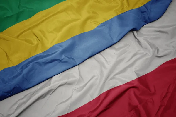 Ondeando colorida bandera de Polonia y bandera nacional de Gabón . — Foto de Stock