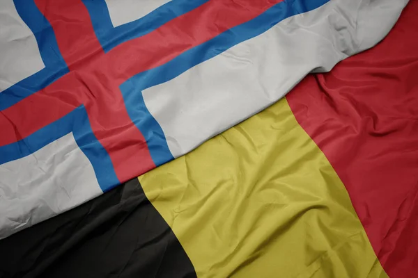 Falująca kolorowa flaga Belgii i flaga narodowa Wysp Owczych. — Zdjęcie stockowe