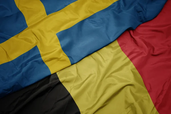 Ondeando colorida bandera de Bélgica y bandera nacional de Suecia . — Foto de Stock