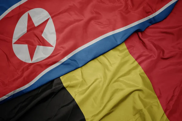 Ondeando colorida bandera de Bélgica y bandera nacional de Corea del Norte . — Foto de Stock