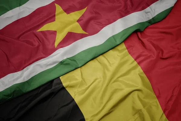 Ondeando colorida bandera de belgium y bandera nacional de surinam . — Foto de Stock
