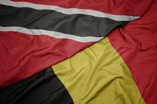 Ondeando colorida bandera de belgium y bandera nacional de trinidad y tobago . — Foto de Stock