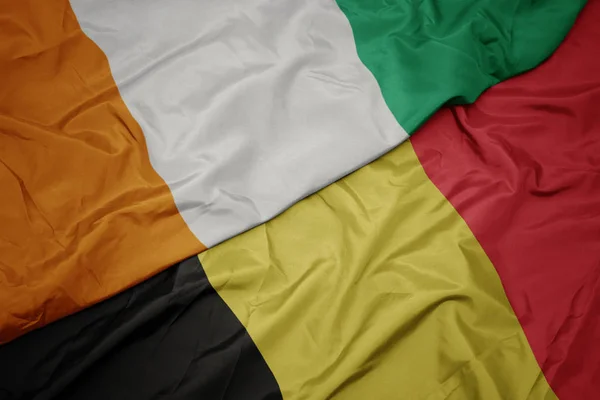 Mávání barevnou vlajkou Belgie a národní vlajky Pobřeží slonoviny. — Stock fotografie