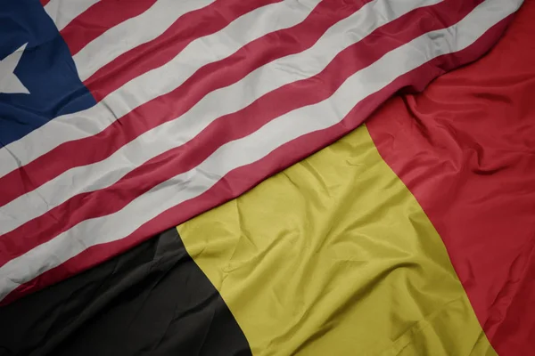 Ondeando colorida bandera de Bélgica y bandera nacional de Liberia . — Foto de Stock