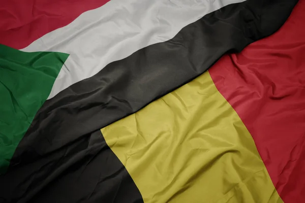Waving colorful flag of belgium and national flag of sudan. — Stock Photo, Image