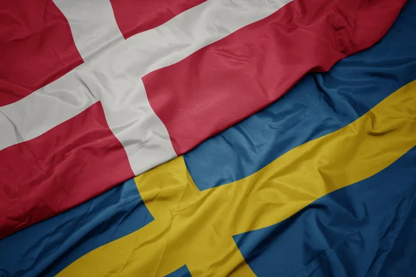 Melambaikan warna-warni bendera sweden dan nasional bendera denmark . — Stok Foto