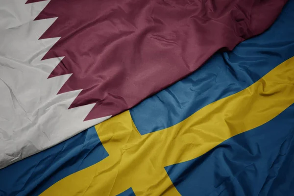 Machanie kolorową flagą Szwecji i flagą narodową Kataru. — Zdjęcie stockowe