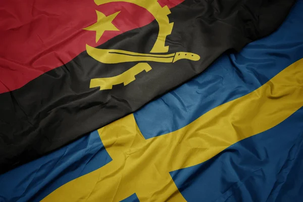 Waving colorful flag of sweden and national flag of angola. — Stock Photo, Image