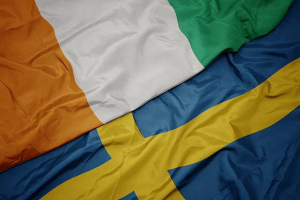 Sventolando bandiera colorata di bandiera svedese e nazionale di cote divoire . — Foto Stock