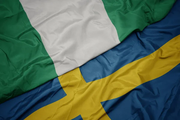 Sventolando bandiera colorata della Svezia e bandiera nazionale della Nigeria . — Foto Stock