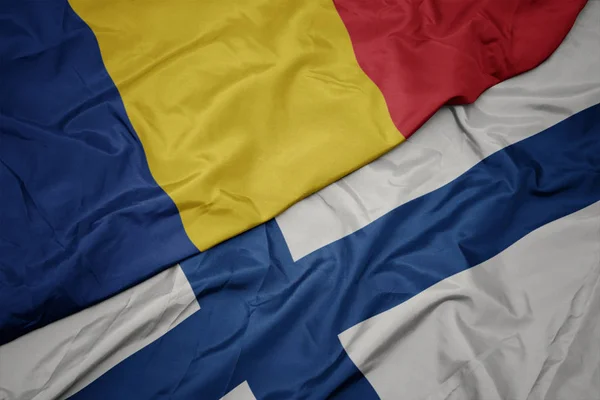 Acenando bandeira colorida da Finlândia e bandeira nacional da Romênia . — Fotografia de Stock