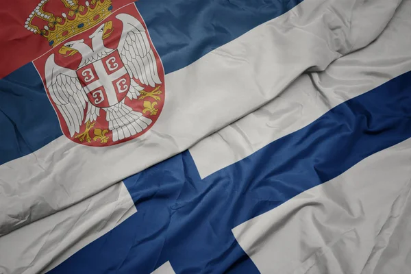 Sventolando bandiera colorata della Finlandia e bandiera nazionale della Serbia . — Foto Stock