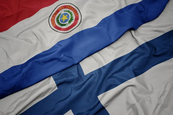 Zwaaiende vlag van Finland en nationale vlag van Paraguay. — Stockfoto