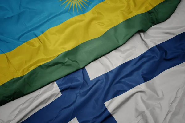 Mávání barevnou vlajkou Finska a národní vlajky Rwandy. — Stock fotografie