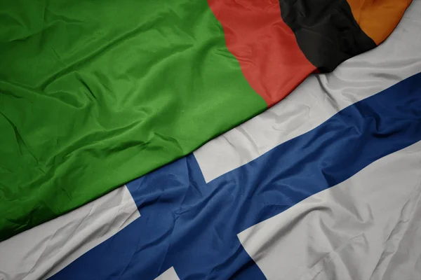 Falująca kolorowa flaga Finlandii i flaga narodowa Zambii. — Zdjęcie stockowe
