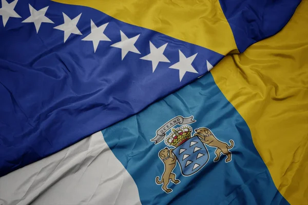 Falująca kolorowa flaga Wysp Kanaryjskich i flaga narodowa Bośni i Hercegowiny. — Zdjęcie stockowe