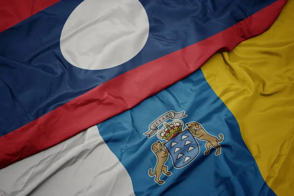 Ondeando colorida bandera de las islas canarias y bandera nacional de laos . —  Fotos de Stock