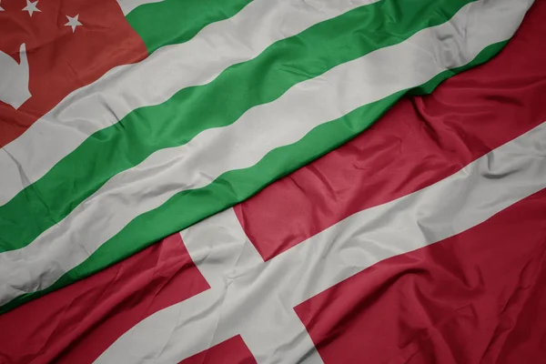 Acenando bandeira colorida de denmark e bandeira nacional da abcásia . — Fotografia de Stock