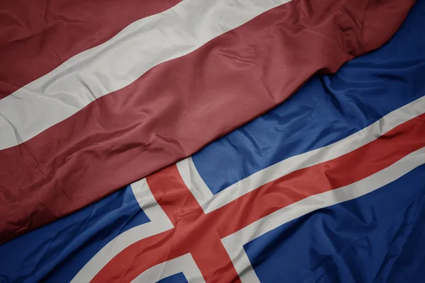 Schwenken bunte Flagge von Island und Nationalflagge von Lettland. — Stockfoto