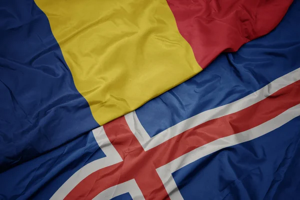 Acenando bandeira colorida da Islândia e bandeira nacional da Romênia . — Fotografia de Stock