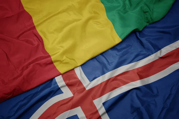 Zwaaiende vlag van IJsland en nationale vlag van Guinee. — Stockfoto