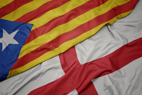 waving colorful flag of england and national flag of catalonia.