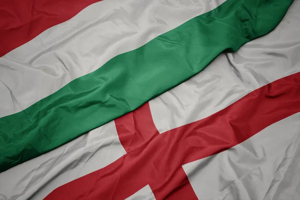 waving colorful flag of england and national flag of hungary.