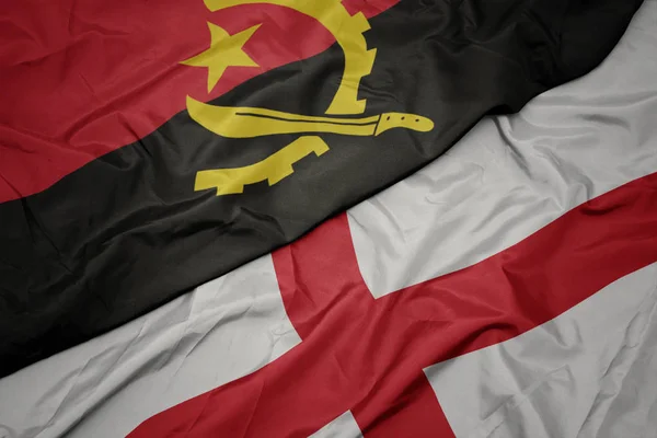 waving colorful flag of england and national flag of angola.