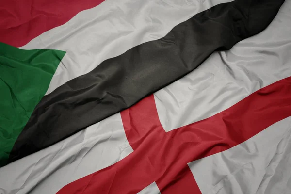 waving colorful flag of england and national flag of sudan.